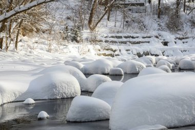 Yoğun karla kaplı büyük kayalar akan bir derede oturur ve yumuşak, yuvarlak şekilli eşsiz bir kış manzarası yaratır..