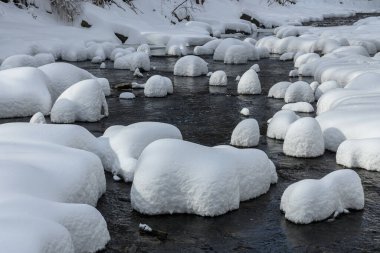 Yoğun karla kaplı büyük kayalar akan bir derede oturur ve yumuşak, yuvarlak şekilli eşsiz bir kış manzarası yaratır..