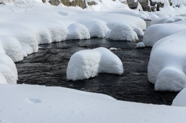 Yoğun karla kaplı büyük kayalar akan bir derede oturur ve yumuşak, yuvarlak şekilli eşsiz bir kış manzarası yaratır..