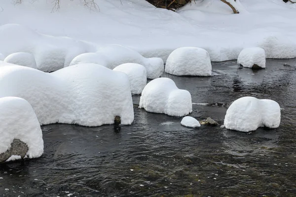 Yoğun karla kaplı büyük kayalar akan bir derede oturur ve yumuşak, yuvarlak şekilli eşsiz bir kış manzarası yaratır..