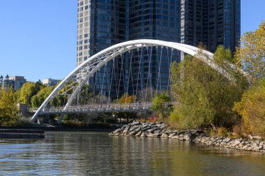 Humber Bay Kemer Köprüsü, arka planda modern bir şehir binasıyla Humber Nehri boyunca kıvrılarak sonbaharda Toronto 'da doğayla harmanlanan kentsel gelişimi gözler önüne seriyor.
