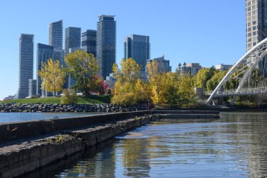 Sonbahar aylarında sakin suyu yansıtan modern yerleşim kulelerinin rıhtım manzarası, Humber Körfezi Kemer Köprüsü ve kıyı boyunca uzanan renkli ağaçların yer aldığı