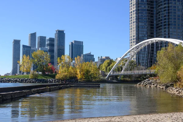 Toronto 'nun Etobikolin kıyısı modern yüksek binaları ve Mimico Deresi üzerindeki ikonik Humber Körfezi Kemer Köprüsü' nü, berrak mavi gökyüzü altında canlı sonbahar yapraklarıyla sergiliyor.