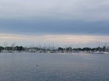 Toronto, ON, Kanada - 25 Eylül 2025: Birçok beyaz yelkenli bulutlu bir gökyüzünün altında, küçük beyaz bir deniz fenerinin yanındaki huzurlu bir marinaya yanaştı.