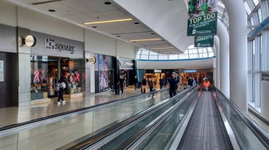 Toronto, ON, Kanada - 12 Ekim 2025: Yolcular geniş pencereli modern bir havaalanı terminali içinde hareket halindeki bir geçitte seyahat ediyorlar.