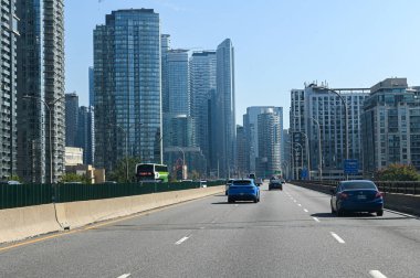 Toronto, Kanada - 30 Eylül 2025: CN Kulesi ve açık mavi gökdelenler altında görünen modern gökdelenlerle şehir merkezindeki bir otoyolda arabalar sürüyor.