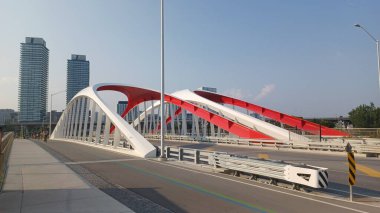 Toronto, ON, Kanada - 6 Temmuz 2025: Sarı kirişli modern bir kemerli köprü, açık ve güneşli bir günde yansımalı bir su kanalı boyunca uzanır.