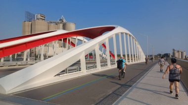 Toronto, ON, Kanada - 6 Temmuz 2025: Sarı kirişli modern bir kemerli köprü, açık ve güneşli bir günde yansımalı bir su kanalı boyunca uzanır.