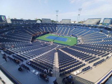 Toronto, ON, Kanada - 23 Ağustos 2025: Güneşli bir günde yeşil bir tenis kortunu çevreleyen boş mavi koltuklu büyük bir stadyum