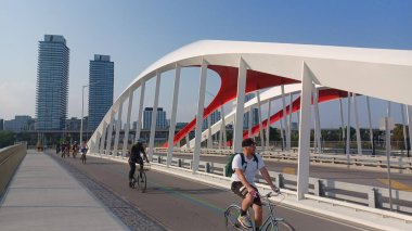 Toronto, ON, Kanada - 6 Temmuz 2025: Sarı kirişli modern bir kemerli köprü, açık ve güneşli bir günde yansımalı bir su kanalı boyunca uzanır.