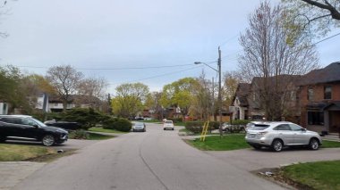 Toronto, ON, Kanada - 26 Nisan 2025: Etobikola 'da bir cadde otomobiller ve tomurcuklanan ağaçlarla banliyö havasını sergiliyor.