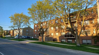 Toronto, ON, Kanada - 26 Nisan 2025: Fotoğraf, bahar aylarında Etobicoke 'da konut binaları ve filizlenen ağaçları gösteren sessiz bir caddeyi resmediyor.