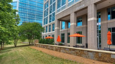 Charlotte, NC, ABD - 30 Nisan 2025: Modern ofis binaları yeşil çimenlerin, ağaçların ve Ballantyne Corporate Park 'ta bulutlu bir gökyüzünün altında bir yürüyüş yolunun ortasında duruyor.