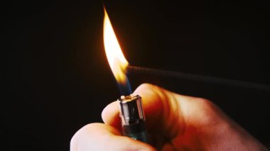 Bir adamın eli, aroma çubuğunu yakan bir çakmağı tutar. Tütsü tütsüsü tütsüsü bir odayı tütsü kokusuyla doldurur. Sadece kokuyu içine çek ve rahatla. Yangın bunu güçlendirir.