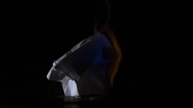 Erkek el bir parça kağıt yakar. Alev alır ve sonunda tamamen yanar. Ateş, sönene kadar ışık ve sıcaklık yayar ve alevler içinde yanmış kül bırakır.