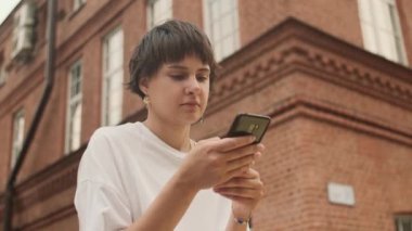 Güzel siyah saçlı genç kız akıllı telefon kullanarak sosyal medyada geziniyor, haberleri kontrol ediyor, mobil oyunlar oynuyor ya da sokaklarda mesajlar yolluyor. Milenyum bayanı. Bulanık çiçekler, şehir arkaplanı