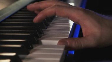 Müzisyen canlı performans sırasında piyano çalar. Sağ el mavimsi bir yıldırımda tuşları çalıyor. Konser izleyicilerinde klavyeci. Piyano çalan bir piyanist midi dijital piyano notaları alır.