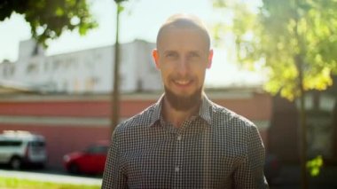 Kel sakallı bir adam az önce kamerayla ya da müfettişle konuştu. Erkek, kameraya gülümsüyor. Güneşli bir günde dışarıda vakit geçiren bir adam. Bulanık şehir, ağaçlar, duvarlar, gökyüzü arkaplanı