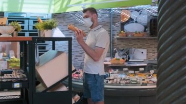 Koruyucu tıbbi maske takan bir adam markette yiyecek, yiyecek ve meyve seçiyor. Toplumsal uzaklık, karantina ve salgının yayılmasına izin vermemek için maske takan bir insan.