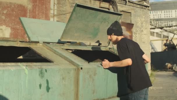 ゴミ捨て場のそばの路上でホームレスの男が食べ物を探している 貧困と惨めさに陥り解雇され解雇され解雇された 社会問題失業概念 — ストック動画