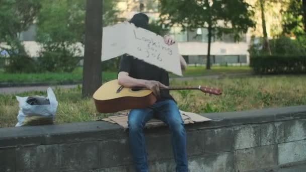 路上で所持品を持つホームレスの男は 仕事を探して ギターを演奏 貧困と惨めさに陥り解雇され解雇され解雇された 社会問題失業概念 — ストック動画