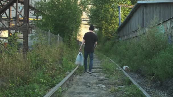 所有物のあるホームレスの男は 鉄道に沿って行く飢えの塊 貧困や惨事に巻き込まれ解雇され解雇され焼かれました 社会問題失業概念 — ストック動画