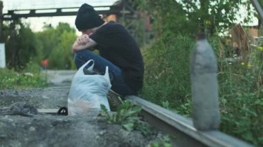 Evsiz bir adam eşyalarıyla uyuyor, demiryolunda oturuyor. Yıkılmış bir insan, fakirlik, sefalet, işten çıkarılma, kovulma, kovulma, tükenme. Sosyal sorunlar, işsizlik kavramı.