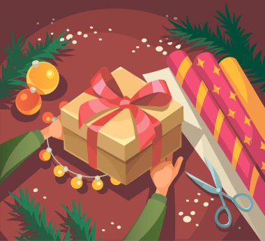 Elinde kırmızı kurdele olan hediye kutusu. Paketleme hediyelerini şık kağıda sarıp kurdeleyle süslemek. Üst görünüm elleri Noel süslemeleri ile masada. El yapımı hediyeler yapmak. Yaratıcı bir hobi..