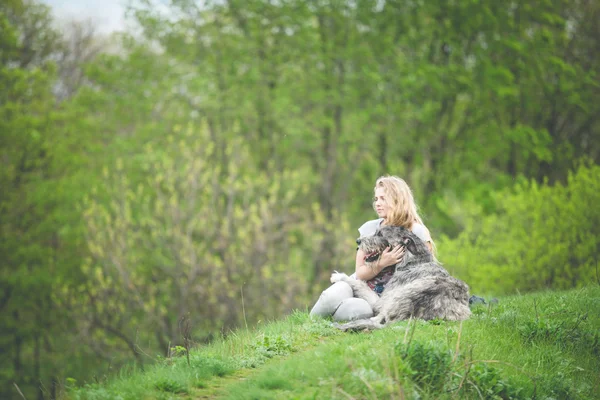 Flickan med det långa ljusa håret kram en enorm grå hund — Stockfoto