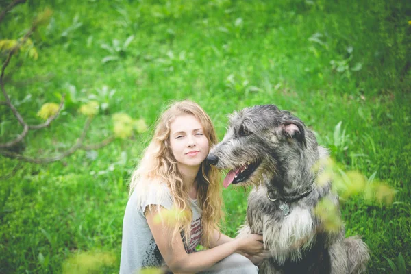 Dziewczyna z siedzieć długie jasne włosy z ogromny pies szary — Zdjęcie stockowe