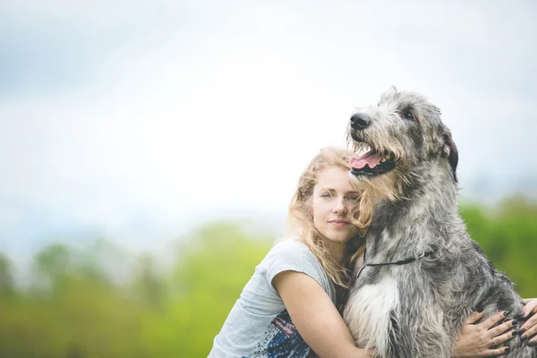 Flickan med det långa ljusa håret kram en enorm grå hund — Stockfoto