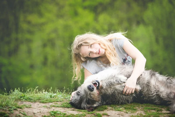 A hosszú világos hajú lány ölelés a hatalmas szürke kutya — Stock Fotó