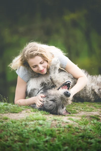 Flickan med det långa ljusa håret kram en enorm grå hund — Stockfoto