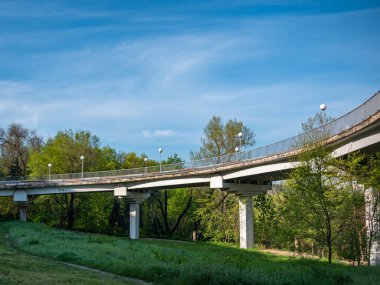 Alçak sütunlardaki otomobil köprüsü ormanın arka planına ve mavi gökyüzüne karşı.