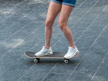 Uzun tahta üzerinde beyaz spor ayakkabılı kadın bacaklarının yakın çekimi. Kız bacaklı kaykay. Gençlik eğlencesi konsepti.