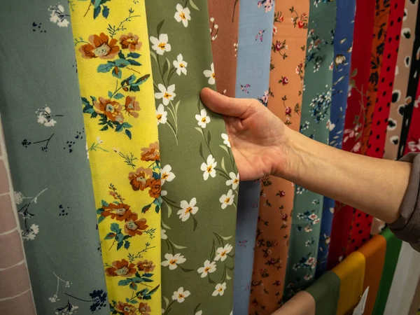 Tekstil salonundaki parlak doğal kumaşların geniş bir çeşitliliği. Bir kadının eli, yeni moda koleksiyonu için örneklerden kumaş seçer..
