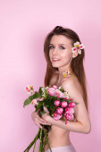 nahá hubená dívka držící květiny na růžovém pozadí. bruneta