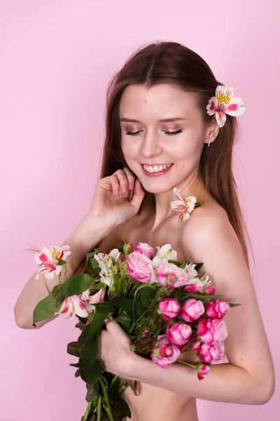 Naken smal flicka som håller blommor på en rosa bakgrund. brunett — Stockfoto