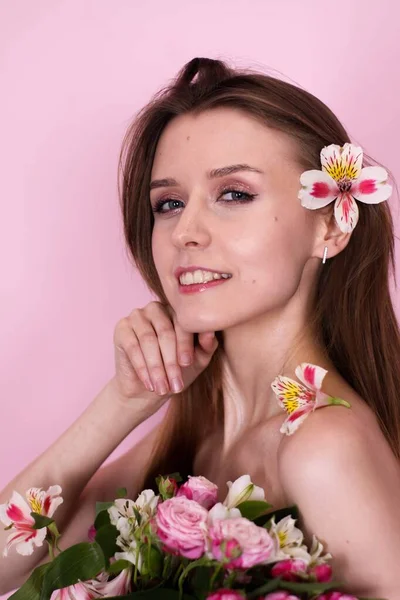 Pembe arka planda çiçek tutan çıplak, sıska bir kız. Esmer.