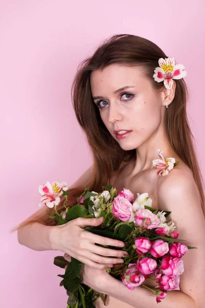 Menina magra nua segurando flores em um fundo rosa. morena — Fotografia de Stock