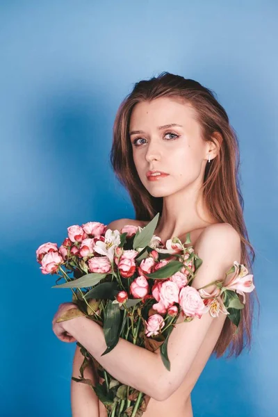 Naakt brunette meisje met bloemen. Natuurlijke schoonheid. op een blauwe achtergrond — Stockfoto