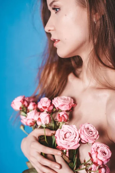 Menina magra nua segurando flores em um fundo rosa. morena — Fotografia de Stock