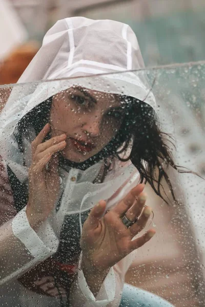 Meisje in de regen in een regenjas. Druppels op glas. — Stockfoto