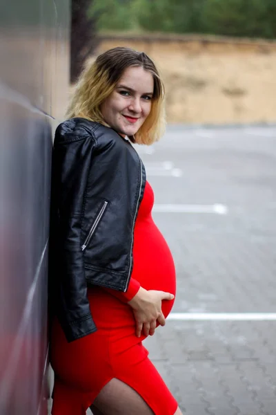 Młoda ciężarna dziewczyna w czerwonej sukience na parkingu. Ciąża to radość. duży brzuch w ciąży. nowe życie. — Zdjęcie stockowe