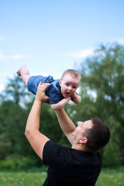 Siyah tişörtlü koyu renk saçlı bir baba oğlunu tarlada tutuyor. Yaz tatili, tatil, aile, mutluluk..