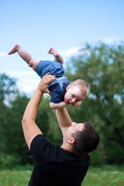 Siyah tişörtlü koyu renk saçlı bir baba oğlunu tarlada tutuyor. Yaz tatili, tatil, aile, mutluluk..