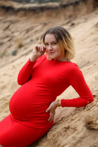 모래 위의 빨간 드레스를 입은 임신 한 소녀. 임신은 즐거운 일입니다. 배가 커요. 새로운 삶. — 스톡 사진