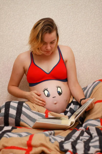 Menina grávida com um rosto desenhado engraçado em seu estômago. — Fotografia de Stock
