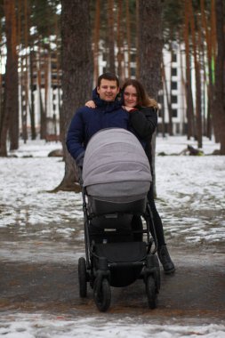 Genç bir aile kışın bebek arabasıyla parkta yürür. Mutlu aile fotoğrafı..