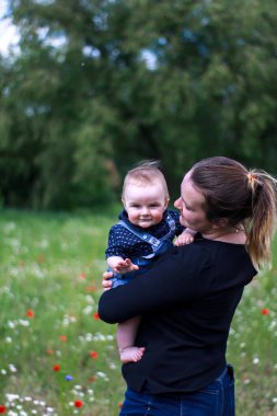 Koyu renk bluzlu bir anne ve tarlada kucağında küçük bir oğlan. Haşhaş tarlası. Doğa, bahar. Yaz günü.